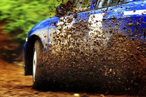 A car sprays mud as it zips around a corner in a dirt road rally